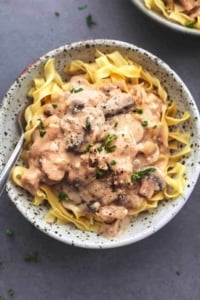 overhead view of saucy brown chicken and mushrooms over noodles in bowl with fork