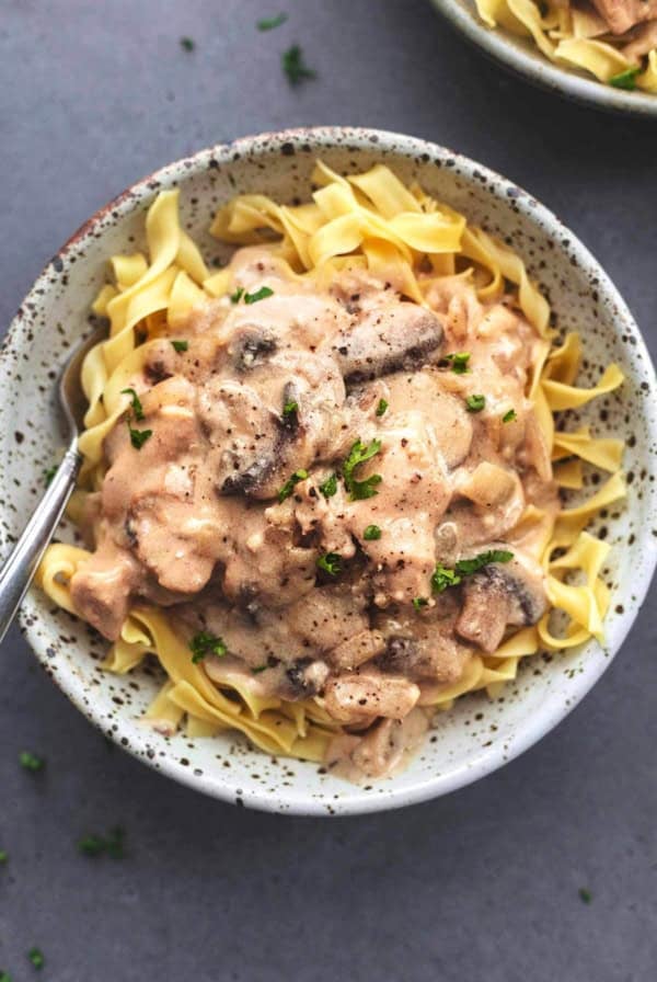 overhead view of saucy brown chicken and mushrooms over noodles in bowl with fork
