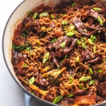 45 degree angle of skillet filled with beef, broccoli and noodles topped with green onions
