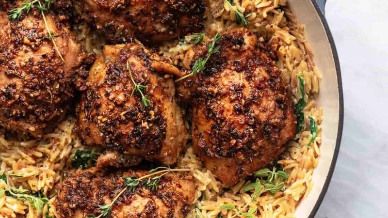 overhead three quarter view of baked chicken and orzo with herbs in a pan