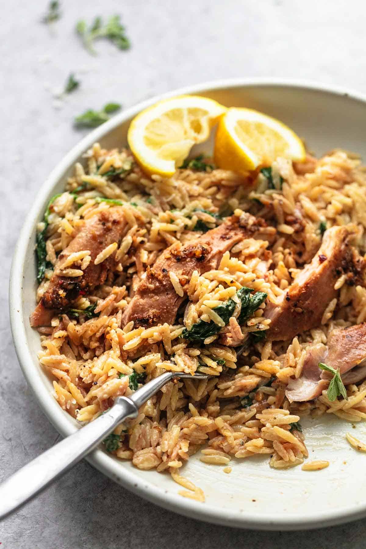 Green chicken and orzo with a fork and lemon slices on a plate.