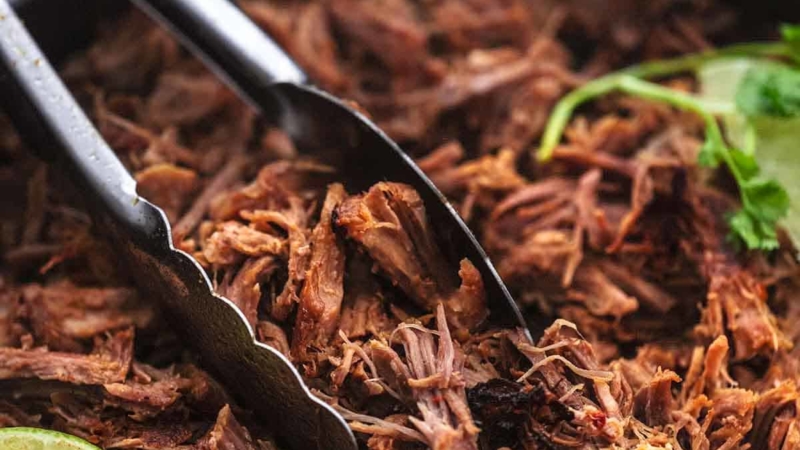 up close shredded pork held by tongs in a skillet