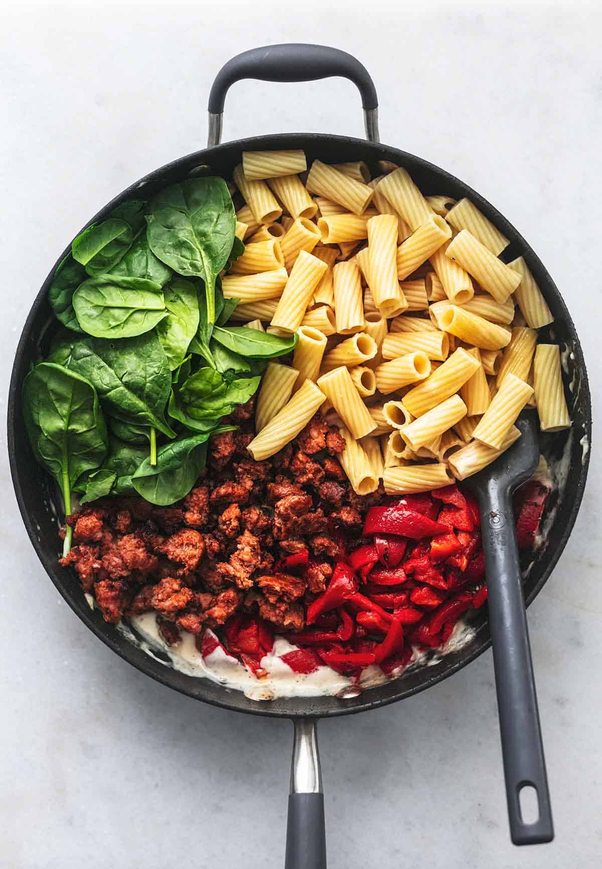 top view of a skillet filled with tuscan sausage pasta ingredients with a serving spoon.