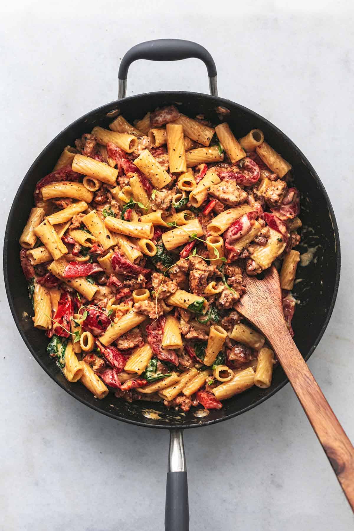 creamy pasta with roasted red peppers in a skillet with wooden spatula