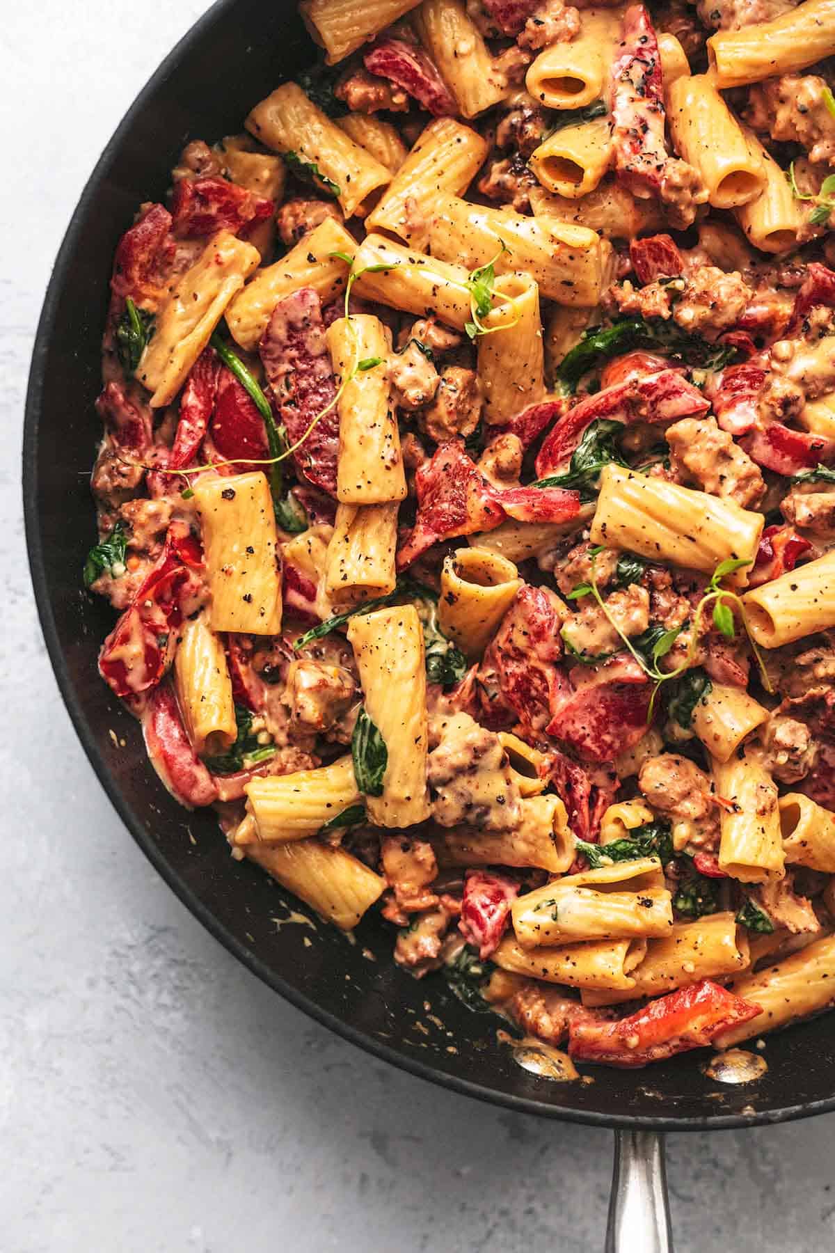 top view of tuscan sausage pasta with fresh thyme on top in a skillet.