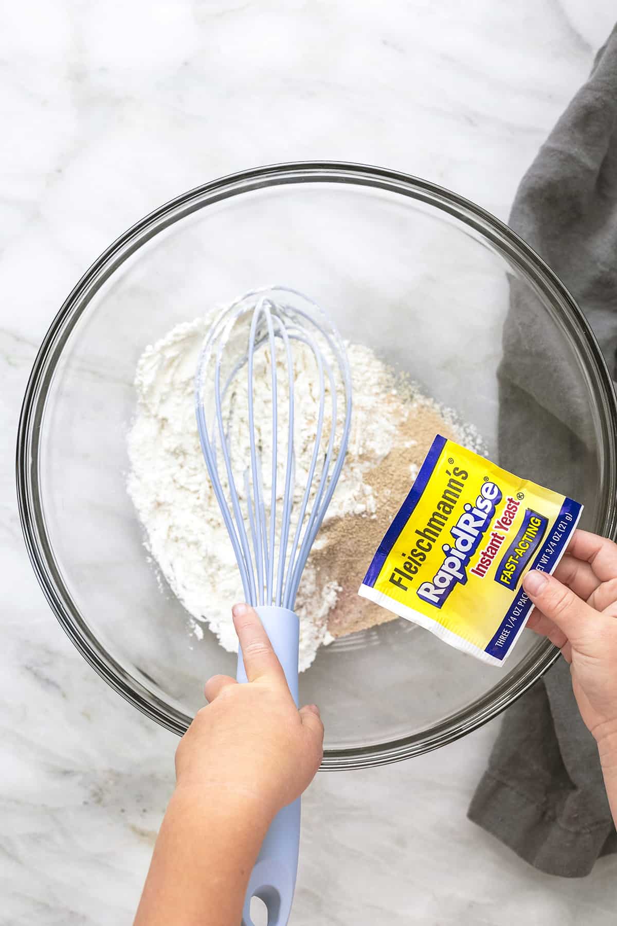 child's hands whisking yeast into a clear glass bowl of flour