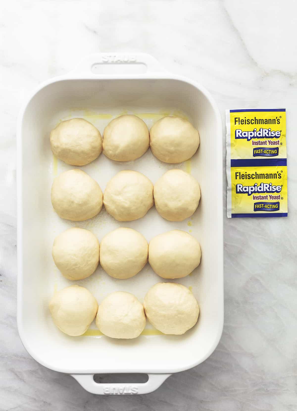 unbaked dough for buttermilk rolls in a baking dish with yeast packets on marble background
