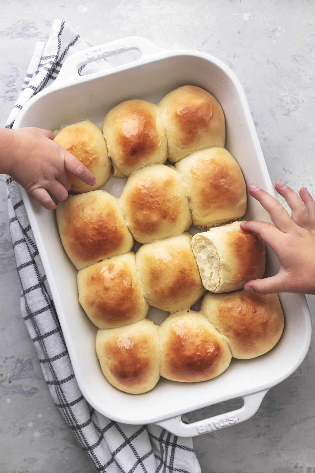 two kids hands reaching to take dinner rolls out of white baking pan