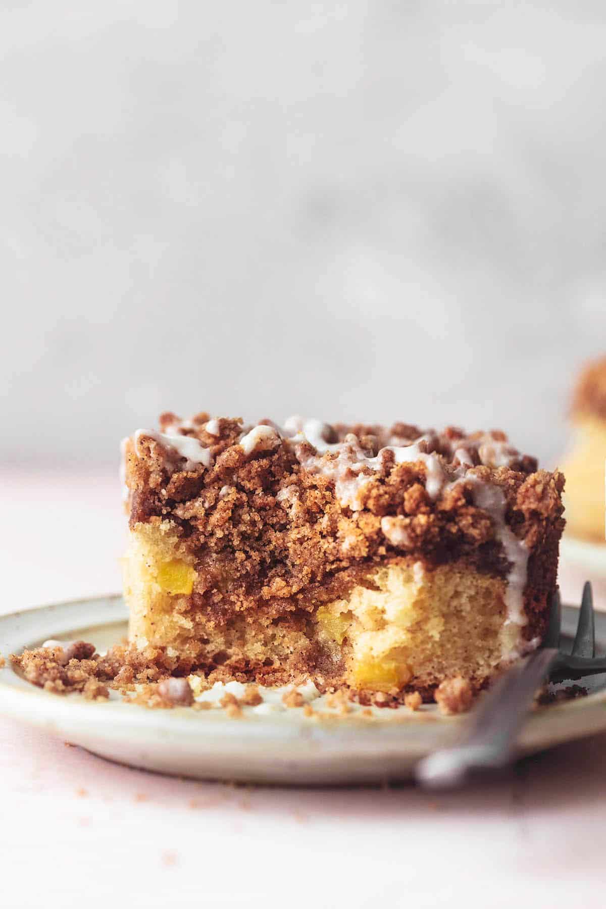 a piece of apple cinnamon coffee cake with a bite missing on a plate with a fork.