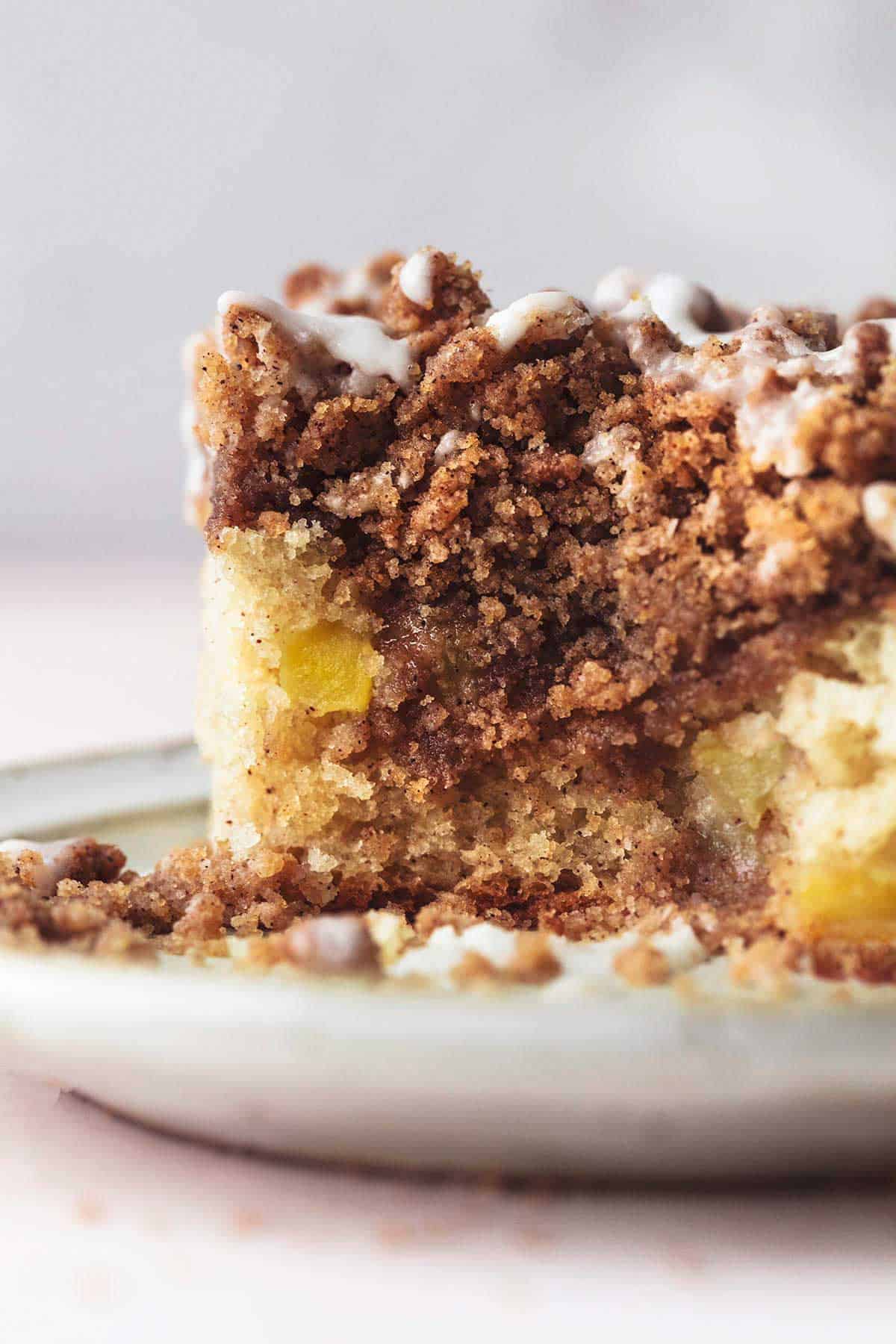 close up of a piece of apple cinnamon coffee cake with streusel filling with a bite missing on a plate.