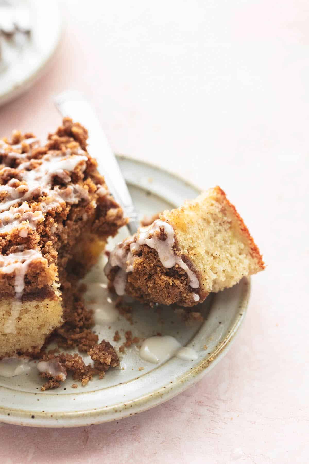 close up of a bite of apple cinnamon coffee cake on a fork with the rest of the piece of cake on the side both on a plate.