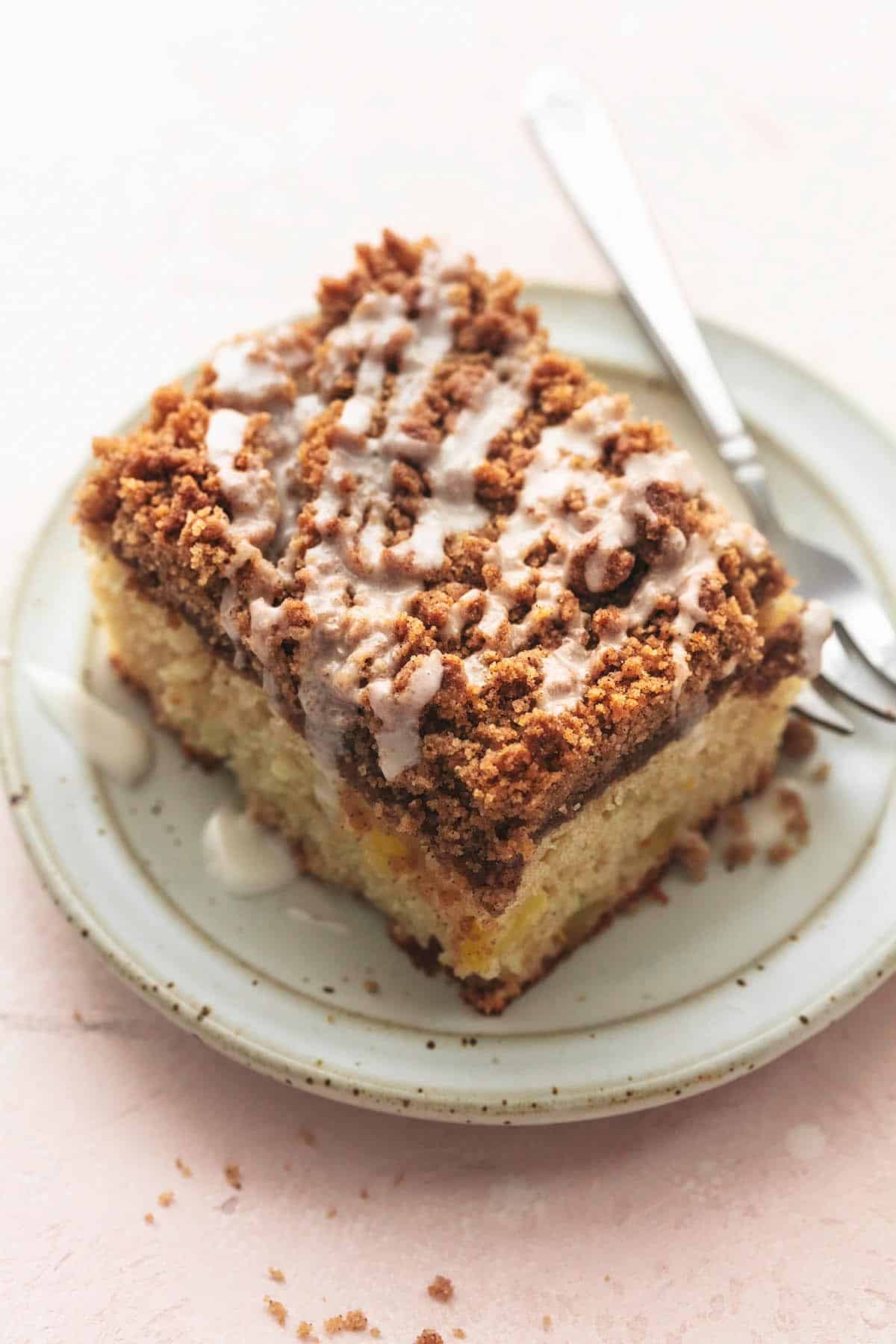 top view of. a piece of apple cinnamon coffee cake with glaze on top on a small plate with fork.