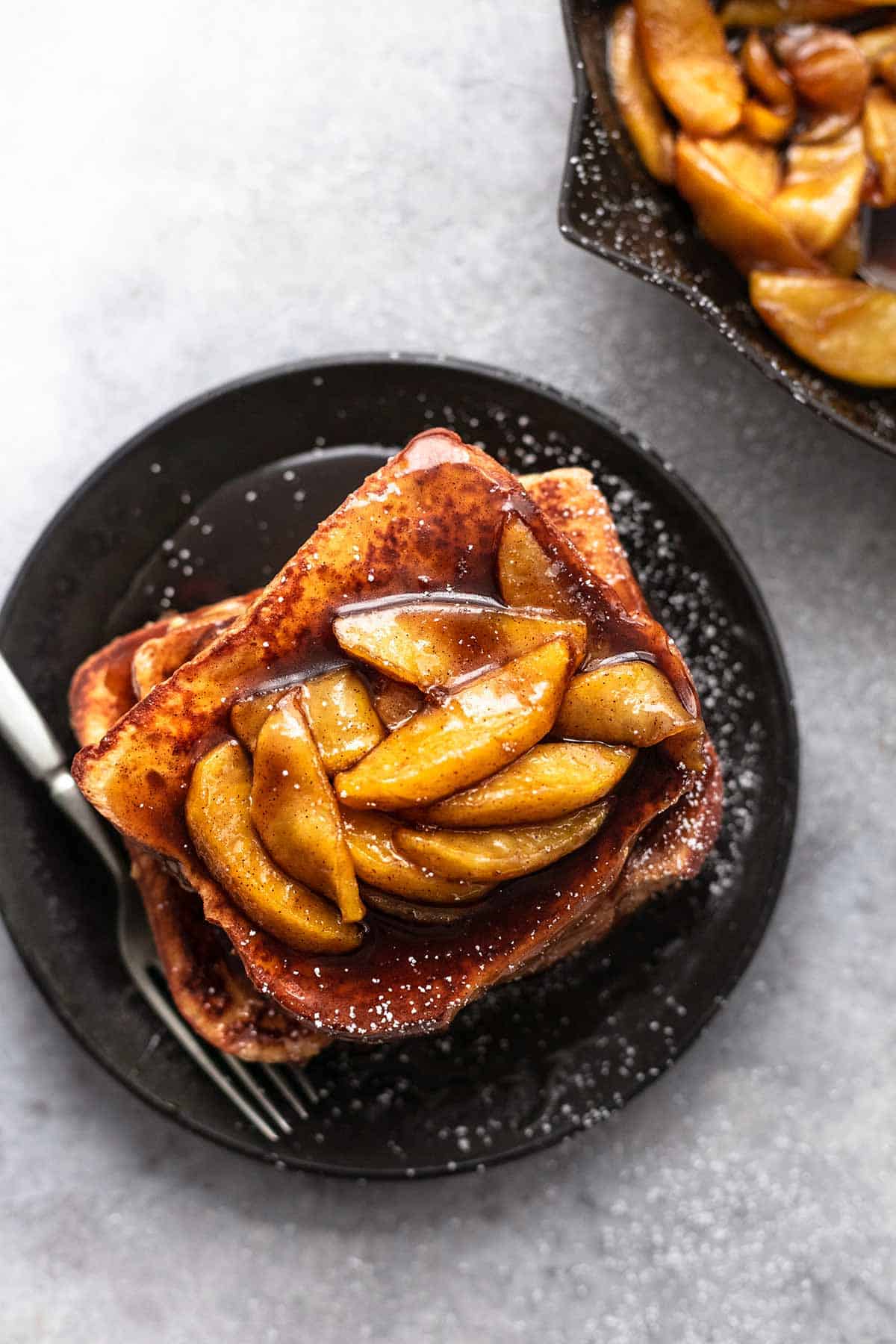 top view of a stack of apple cinnamon french toast topped with apple slices and sauce on a black plate with a fork.