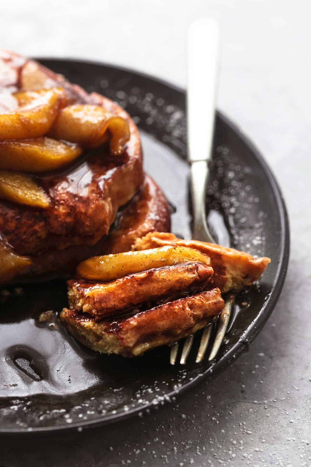 close up of a bite of apple cinnamon French toast on a fork with the rest of the toast on the side with apples and syrup both on a plate.