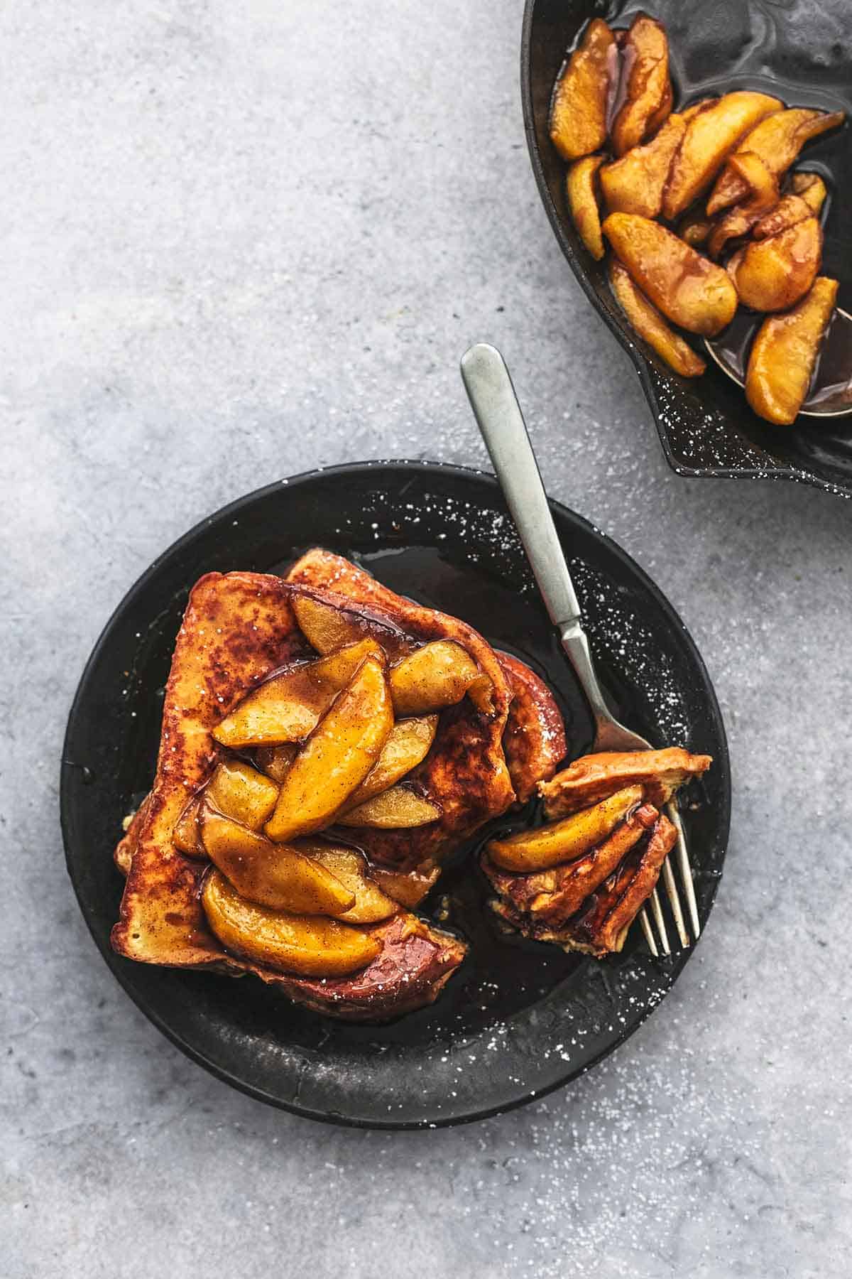 top view of apple cinnamon French toast topped with apple slices and sauce with a bite on a fork both on a plate.