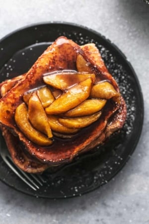 overhead view of stacked french toast topped with apple slices and sauce on a black plate