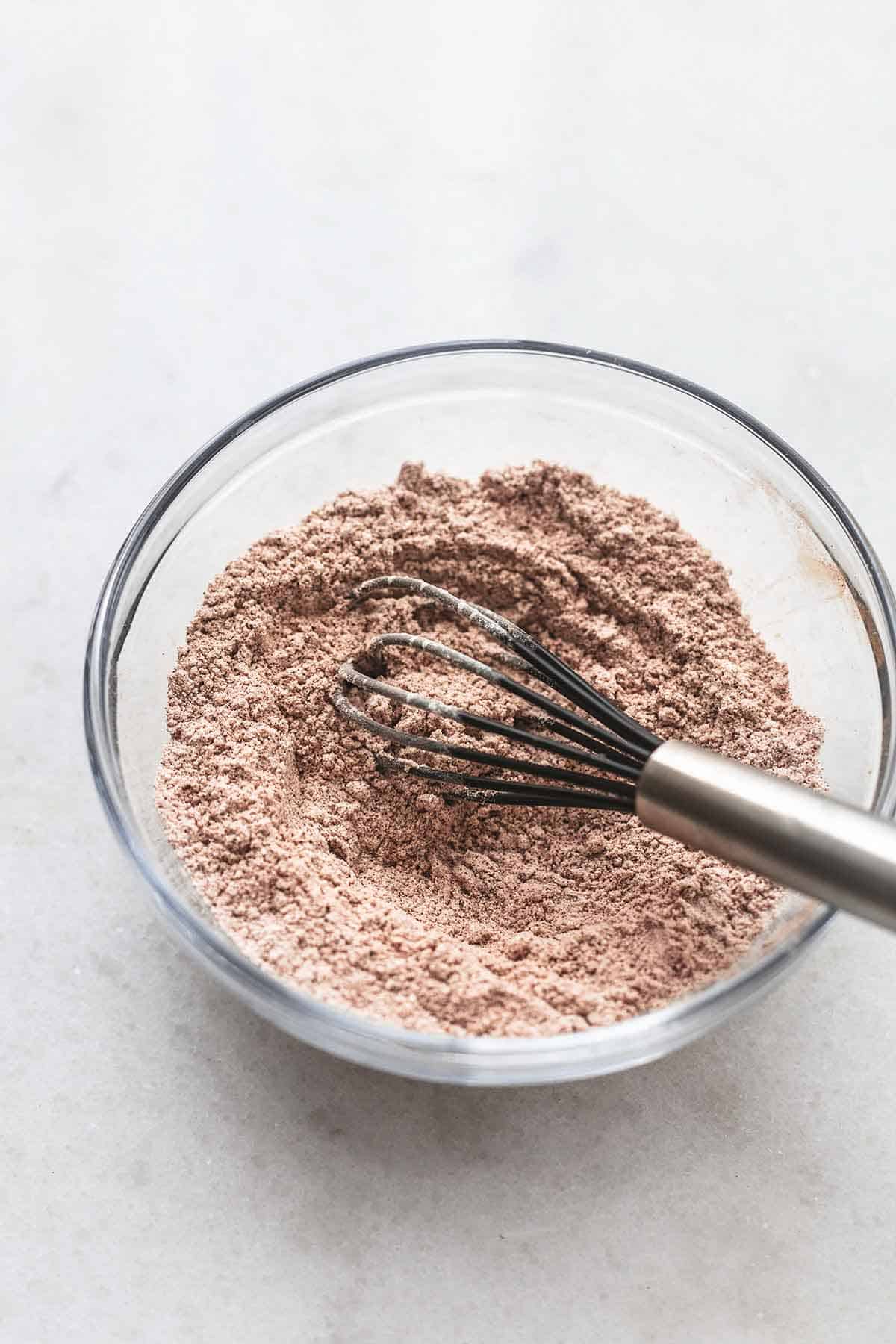 brown colored sugar and flour mixture in a glass bowl with a silver and black rubber whisk.