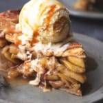 45 degree angle view of single slice of apple pie topped with vanilla ice cream melting down the side