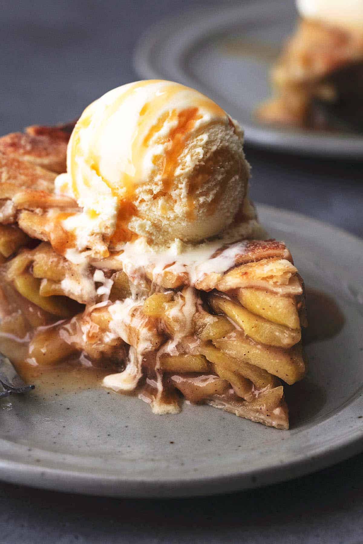 close up of a slice of apple pie topped with vanilla ice cream melting down the side on a plate.