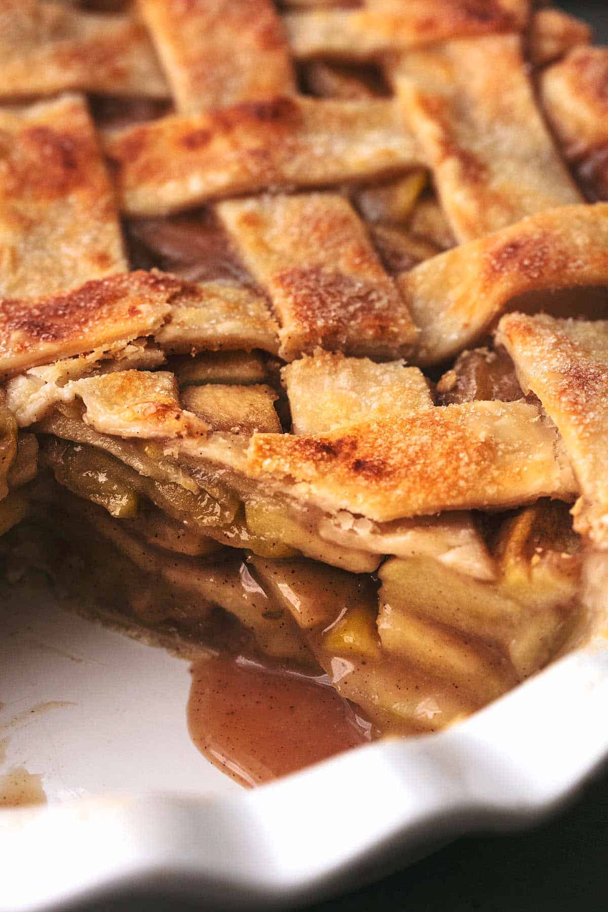 close up of apple pie with lattice top in a white pie dish missing a slice.