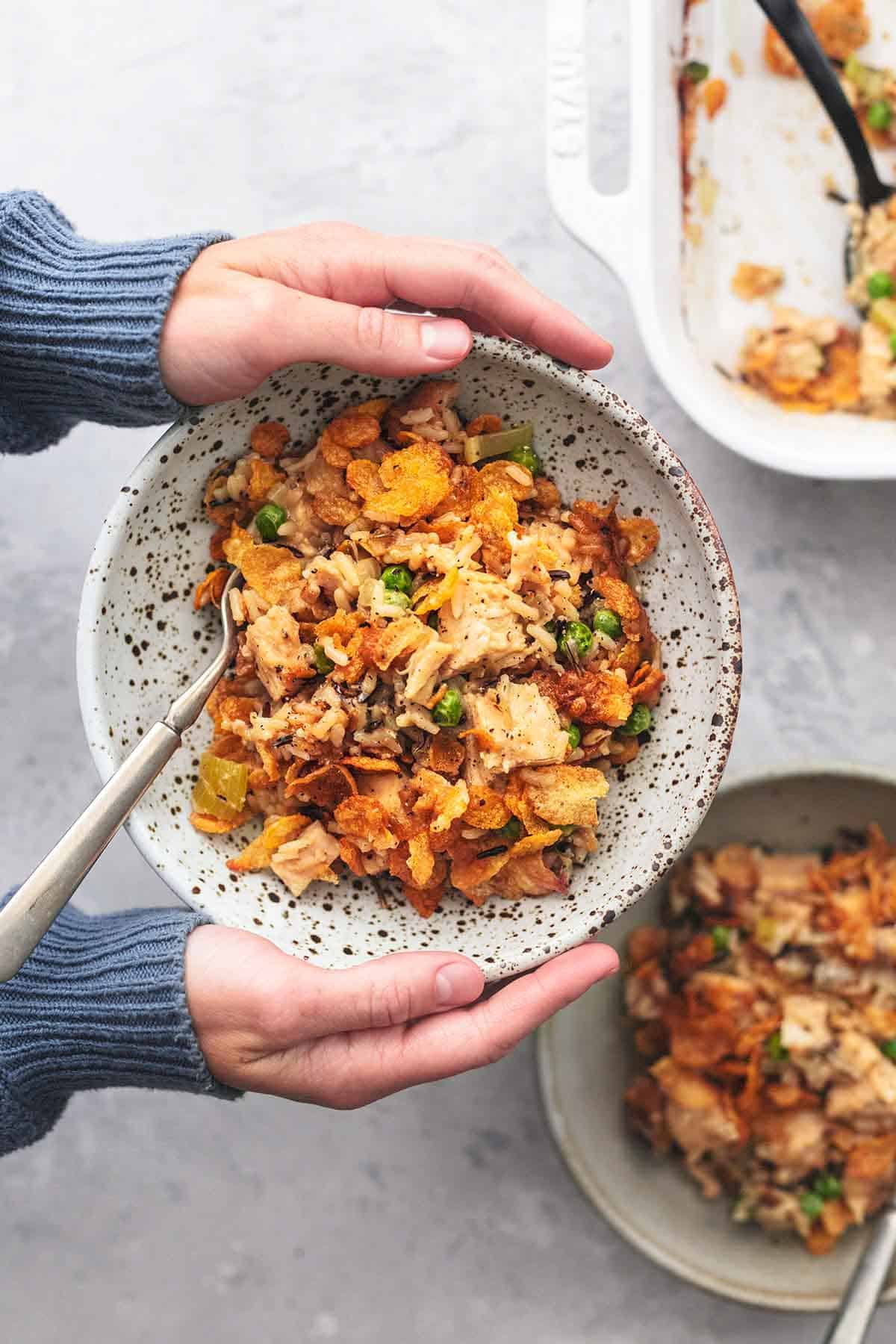 overhead view of hands holding bowl of chicken casserole above another bowl and baking dish