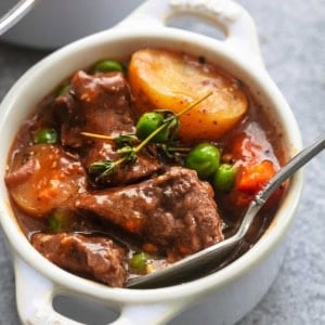 up close view of beef, potatoes, peas, carrots, in thick brown sauce with spoon in mini coquette