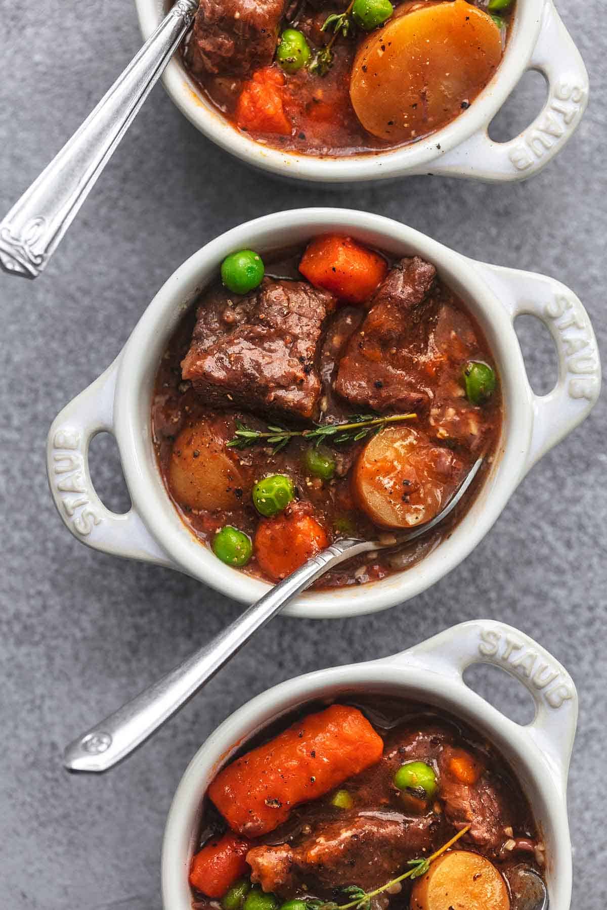 top view of three mini white coquettes filled with beef stew with spoons.