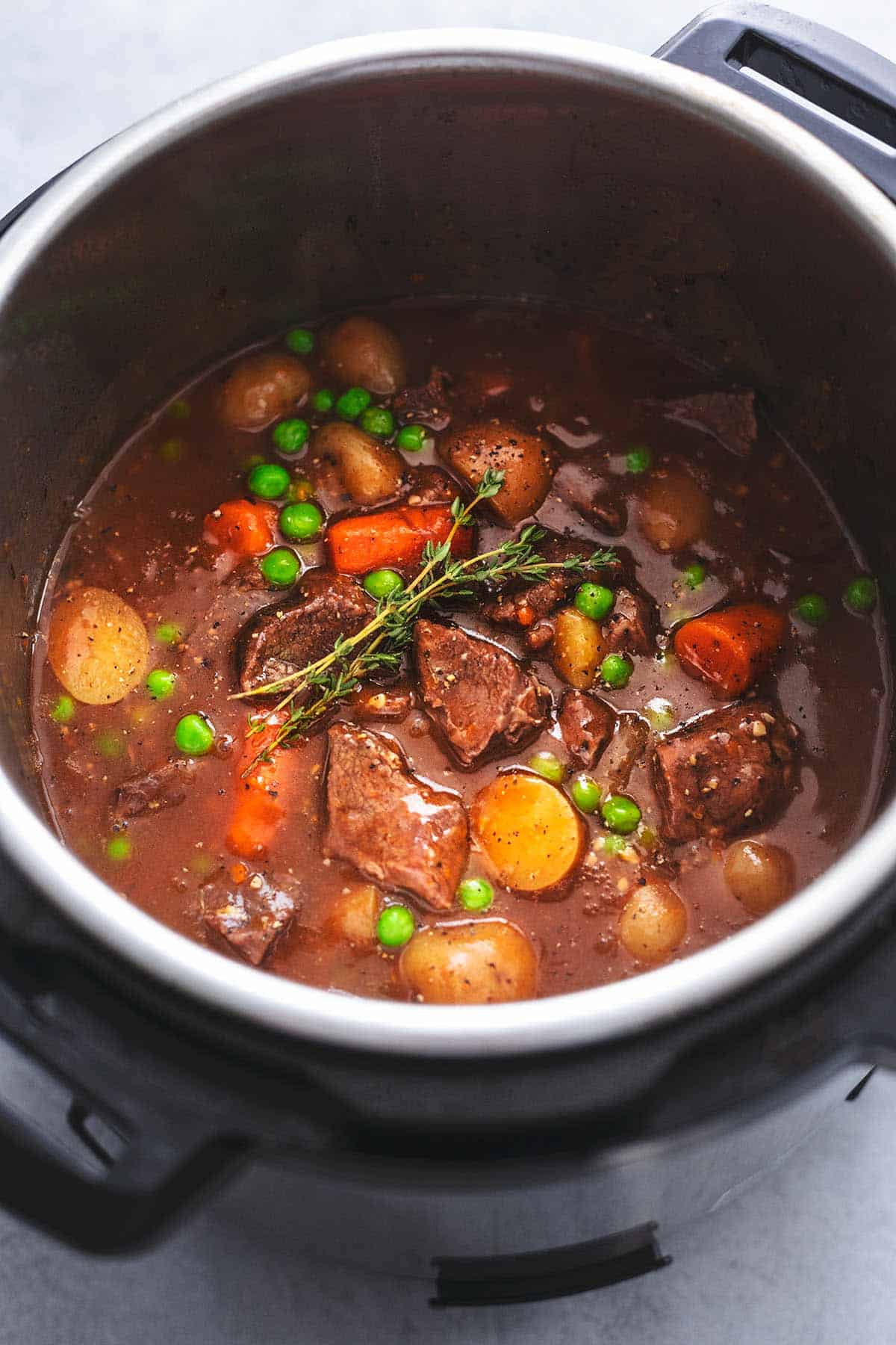 view of inside of pressure cooker pot showing brown sauce with potatoes, carrots, beef chunks, peas, and potatoes