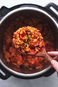 overhead view of hand holding wooden serving spoon with rice and sausage over instant pot