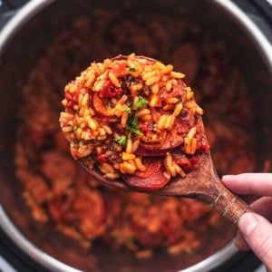 overhead view of hand holding wooden serving spoon with rice and sausage over instant pot