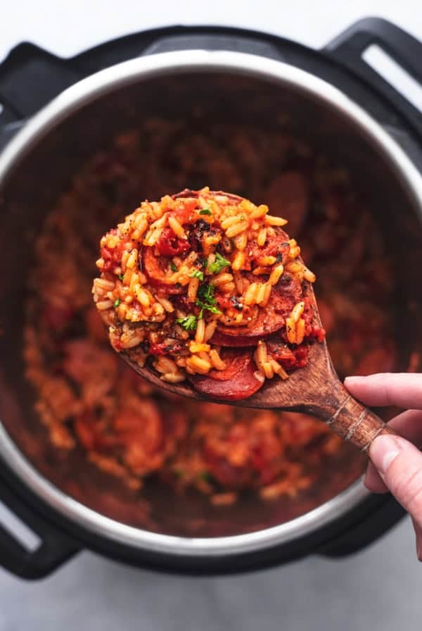 overhead view of hand holding wooden serving spoon with rice and sausage over instant pot