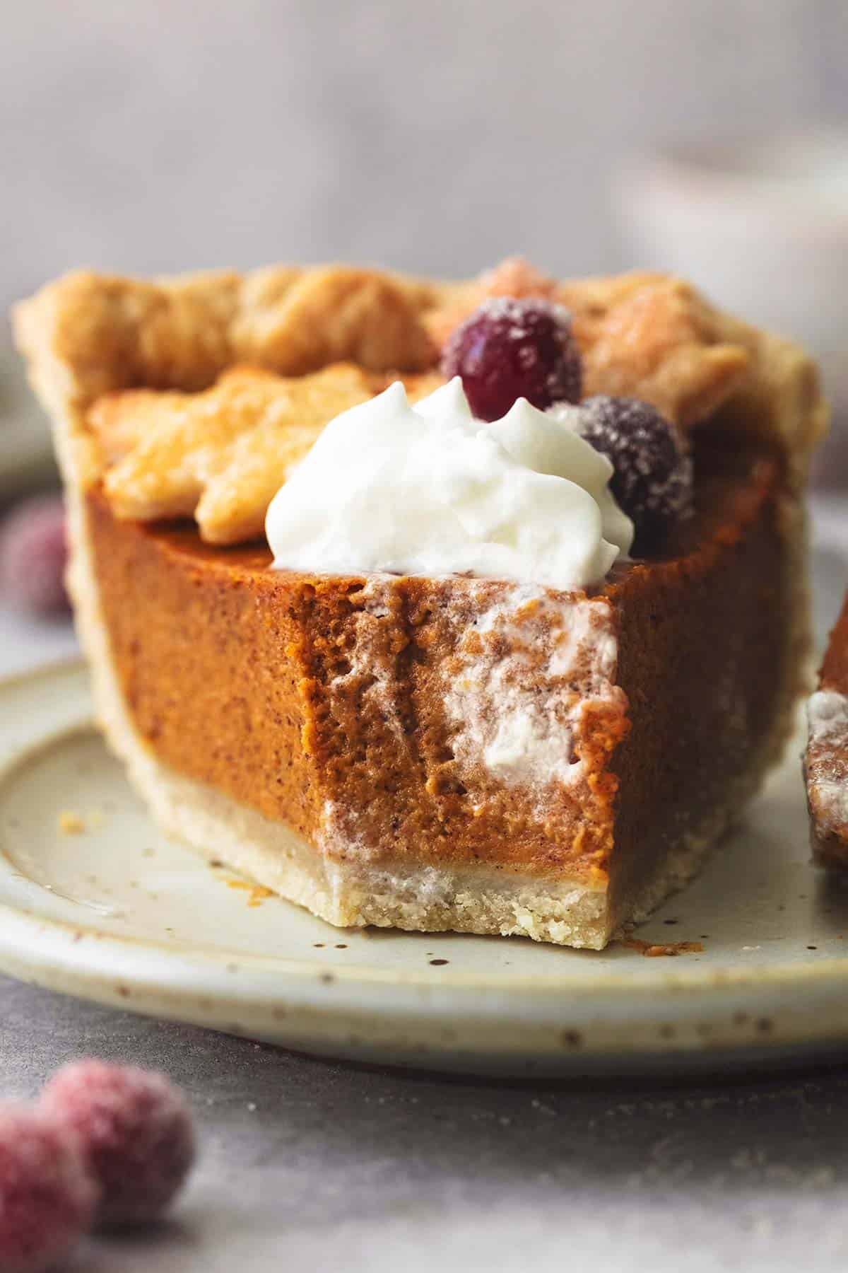 a slice of pumpkin pie with a bite missing with sugared cranberries and cream on top on a plate.
