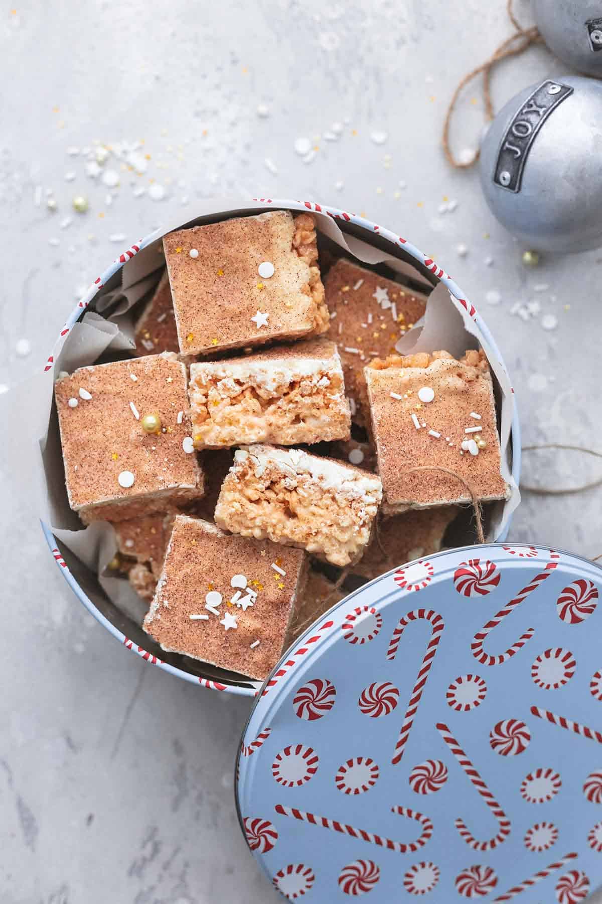 top view of churro Krispie bars in a holiday tin with ornaments on the side.