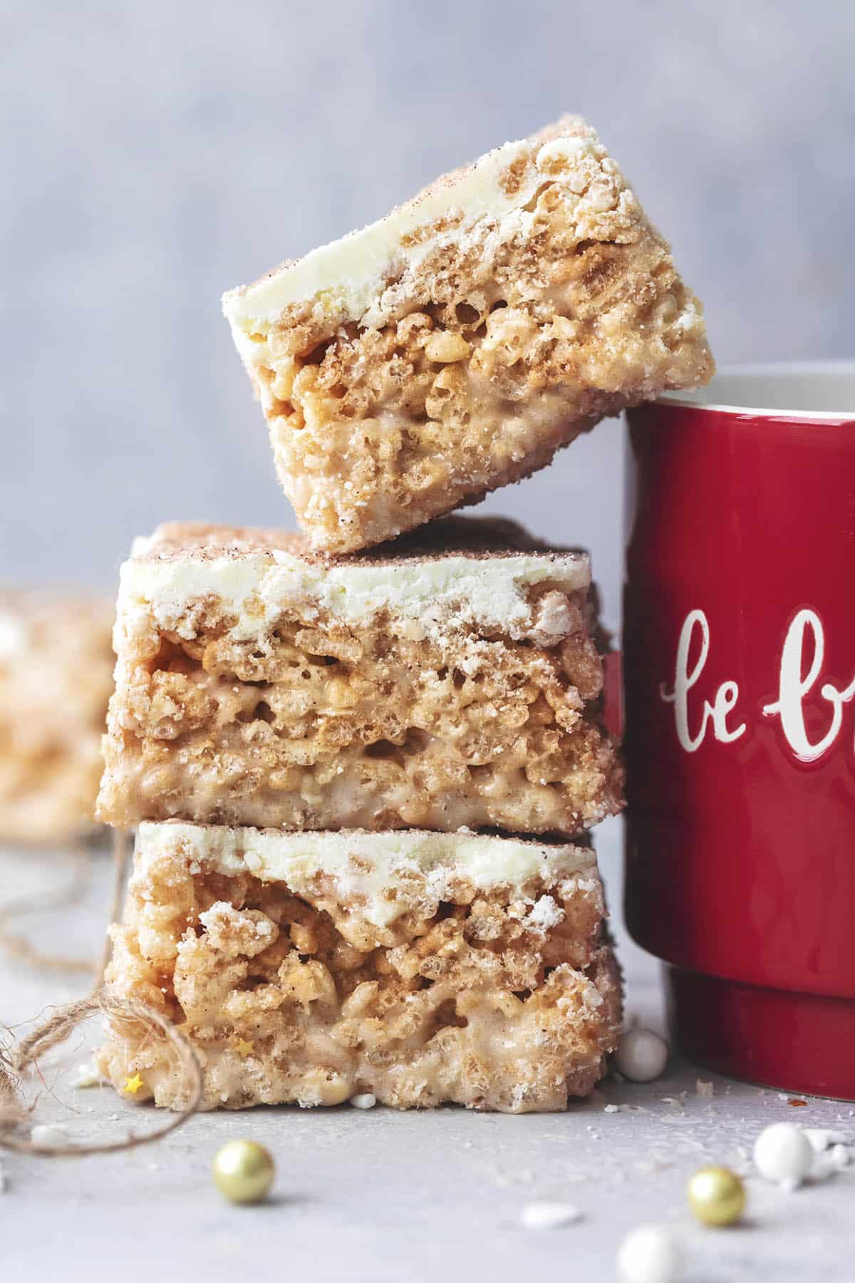 close up of a stack of churro Krispie bars with the top bar leaning on a mug of hot chocolate.