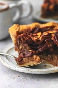 up close bite of apple pecan pie on fork with rest of slice and hot cocoa behind