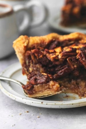 up close bite of apple pecan pie on fork with rest of slice and hot cocoa behind