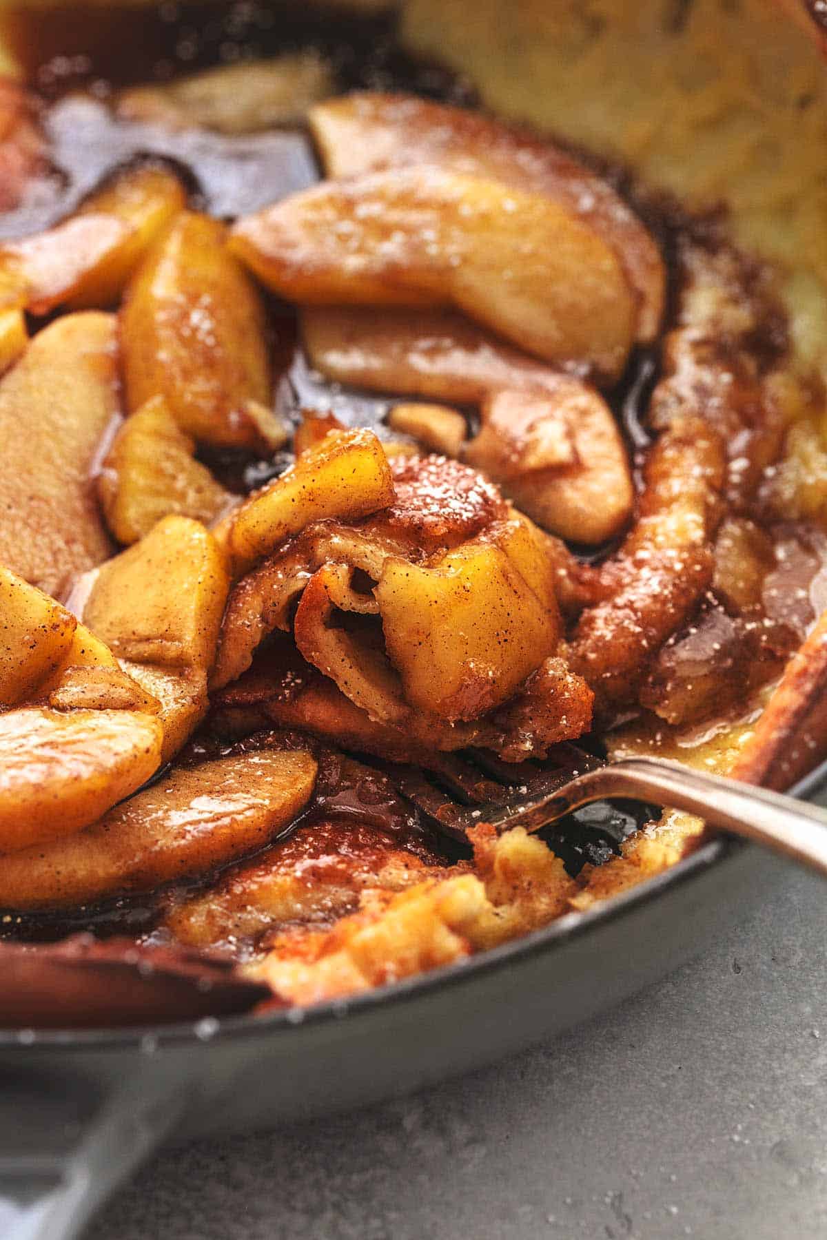 close up of a fork digging into apple dutch baby in a skillet.
