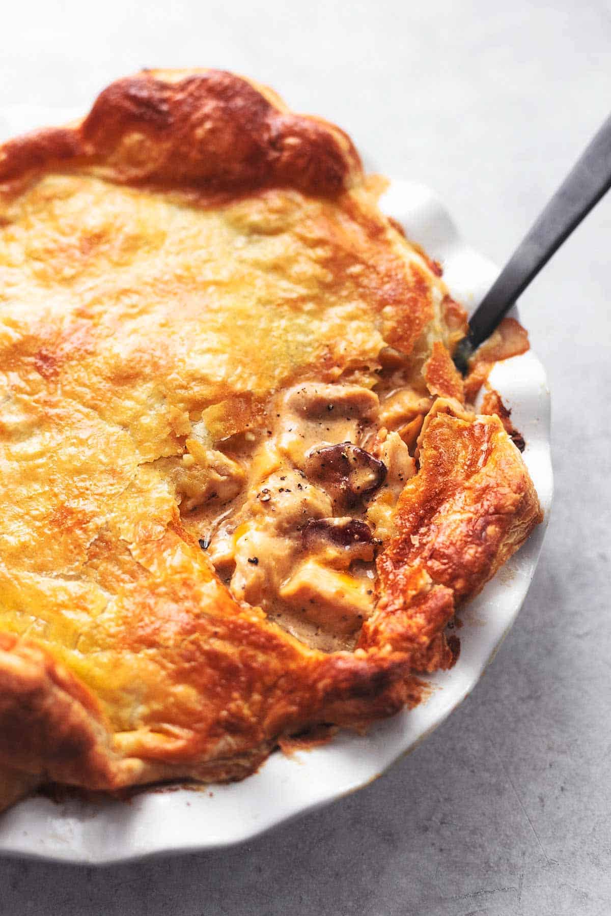 close up of chicken and mushroom pie with a black serving spoon in a white pie dish.