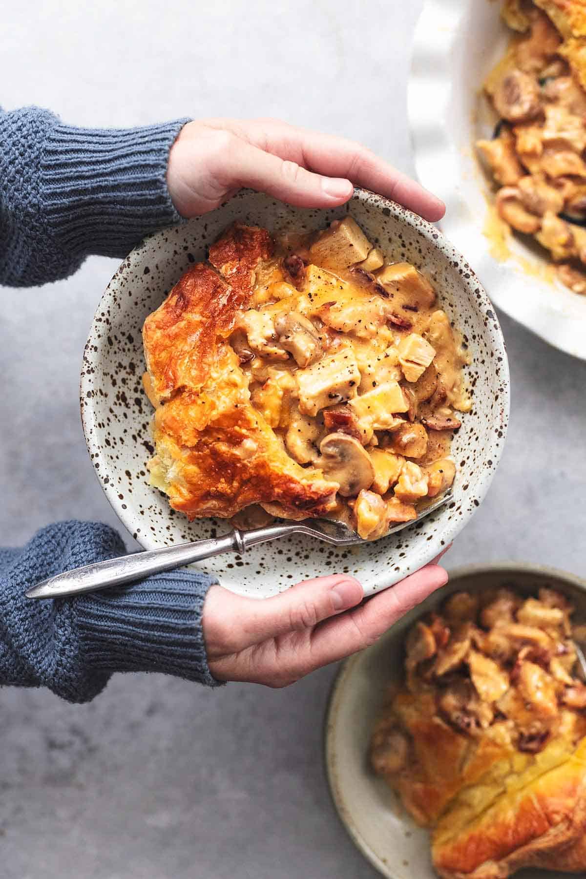 top view of hands holding a bowl of chicken and mushroom pie.