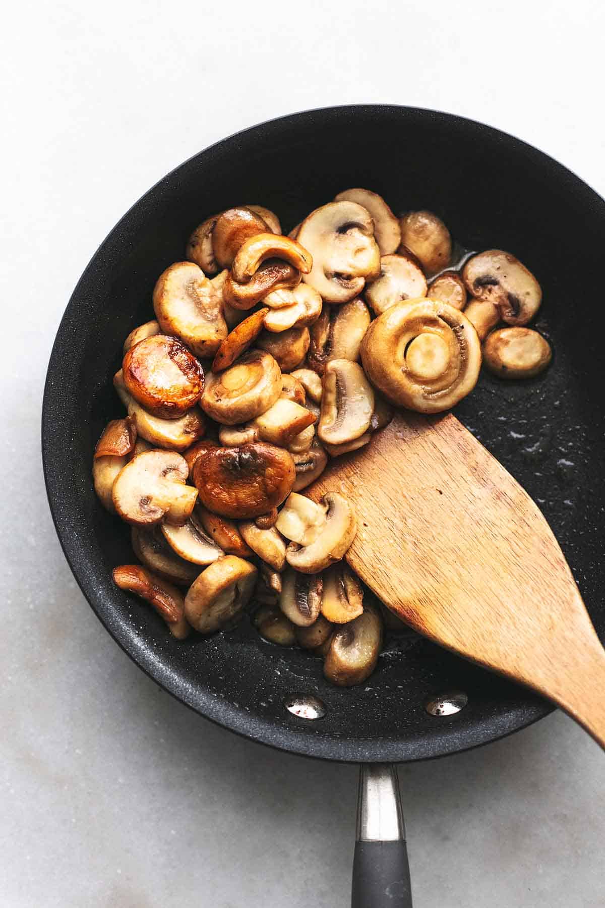 top view of sautéed mushrooms in a black pan with a wooden spoon.