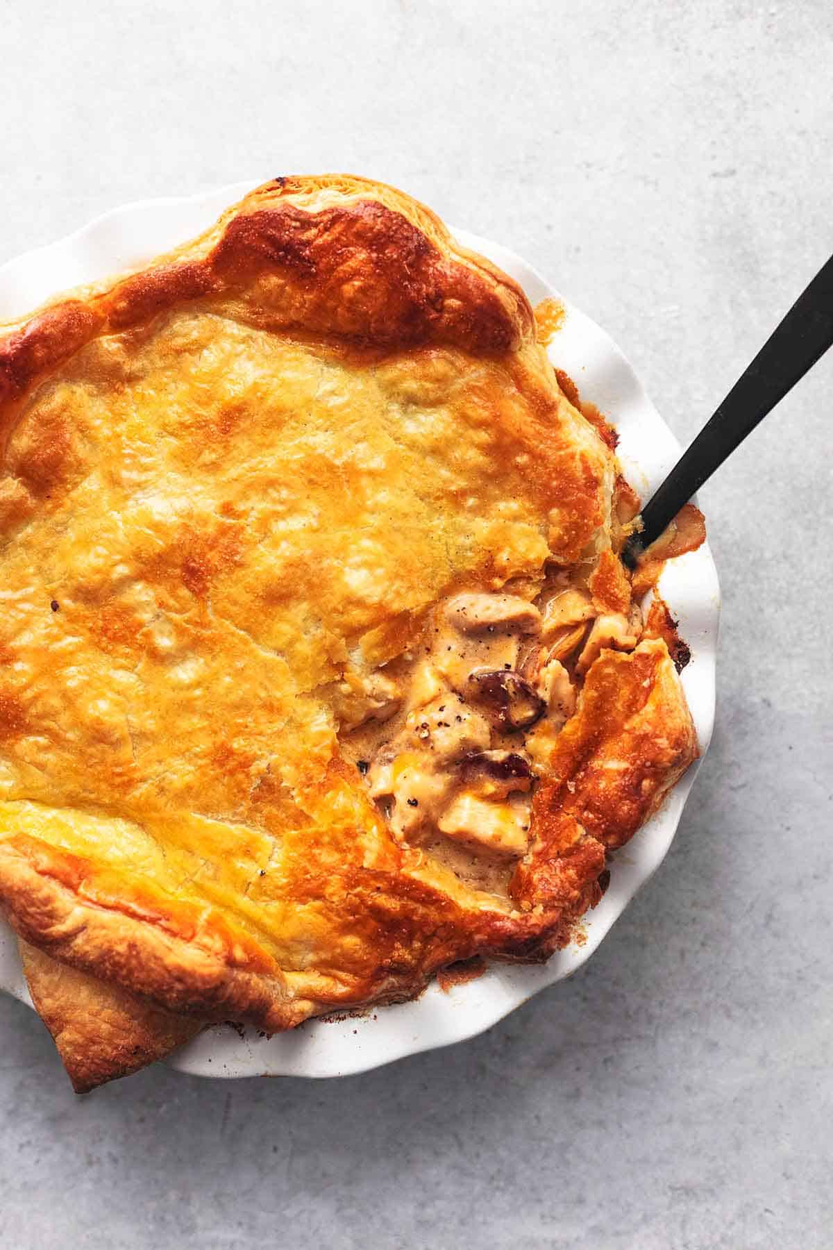 overhead view of white pie dish topped with golden puff pastry and spoon in the dish