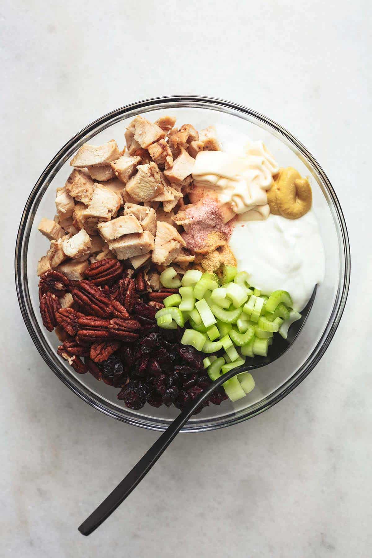 celery, turkey, greek yogurt, pecans, dried cranberries and seasonings in clear glass bowl