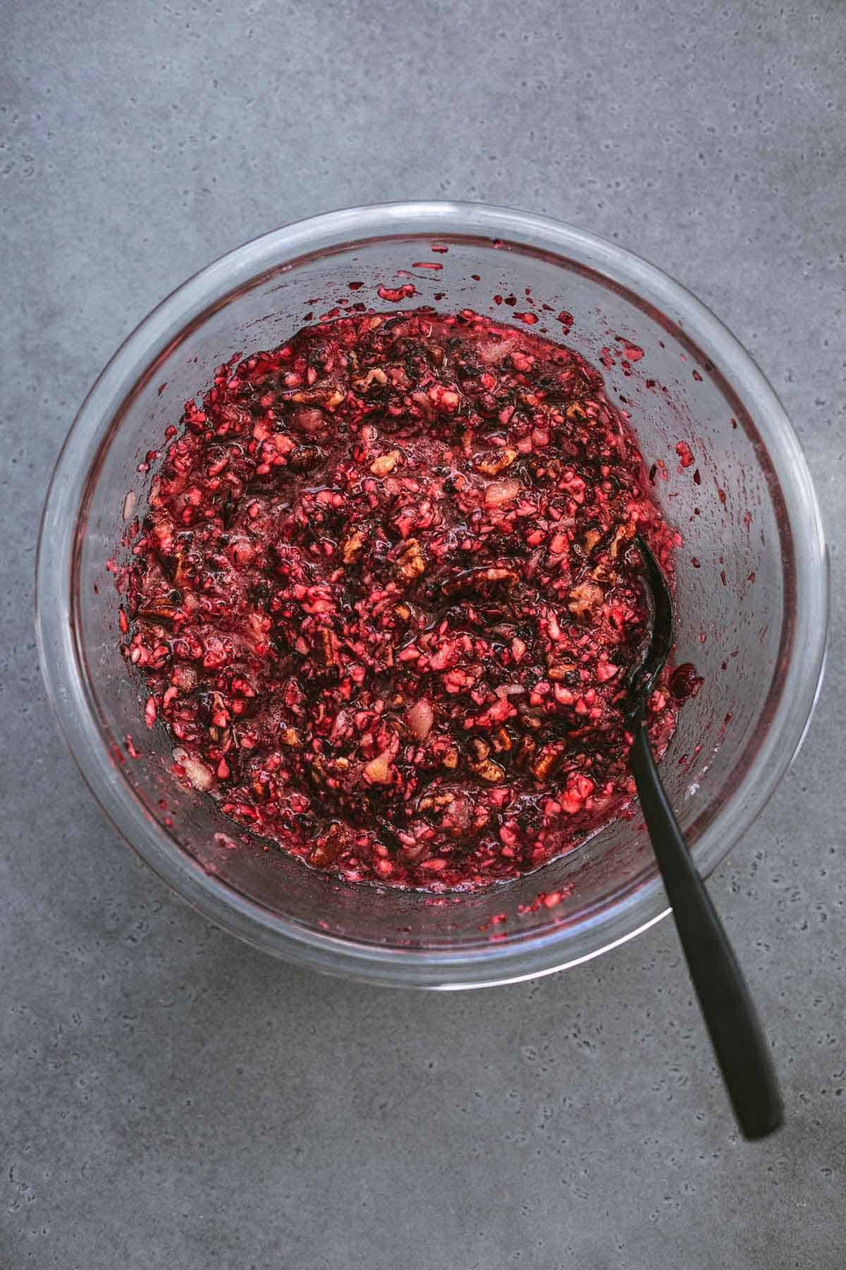 top view of finely chopped red berries and nuts in a glass bowl with a black serving spoon.