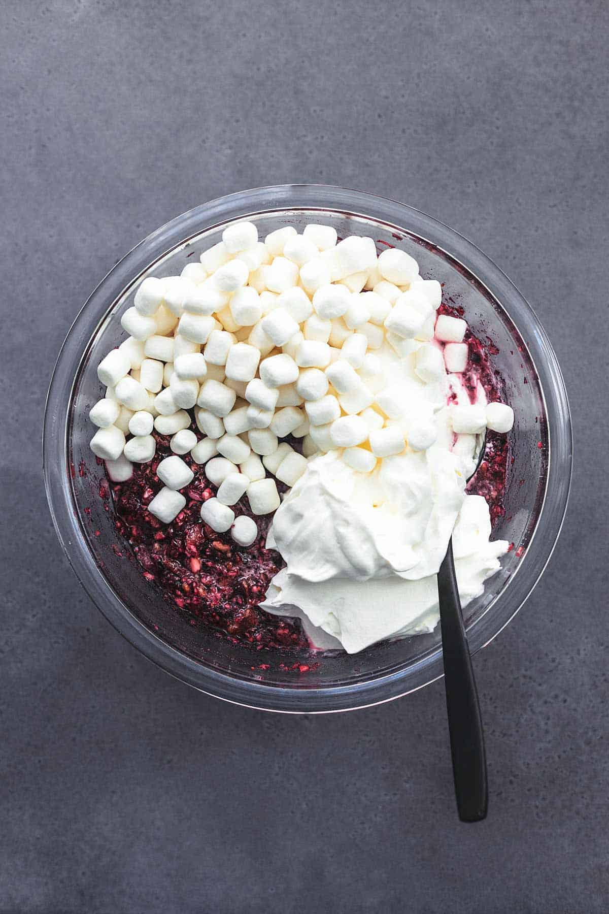 top view of a glass bowl filled with whipped cream, marshmallows, cranberries, and nuts.