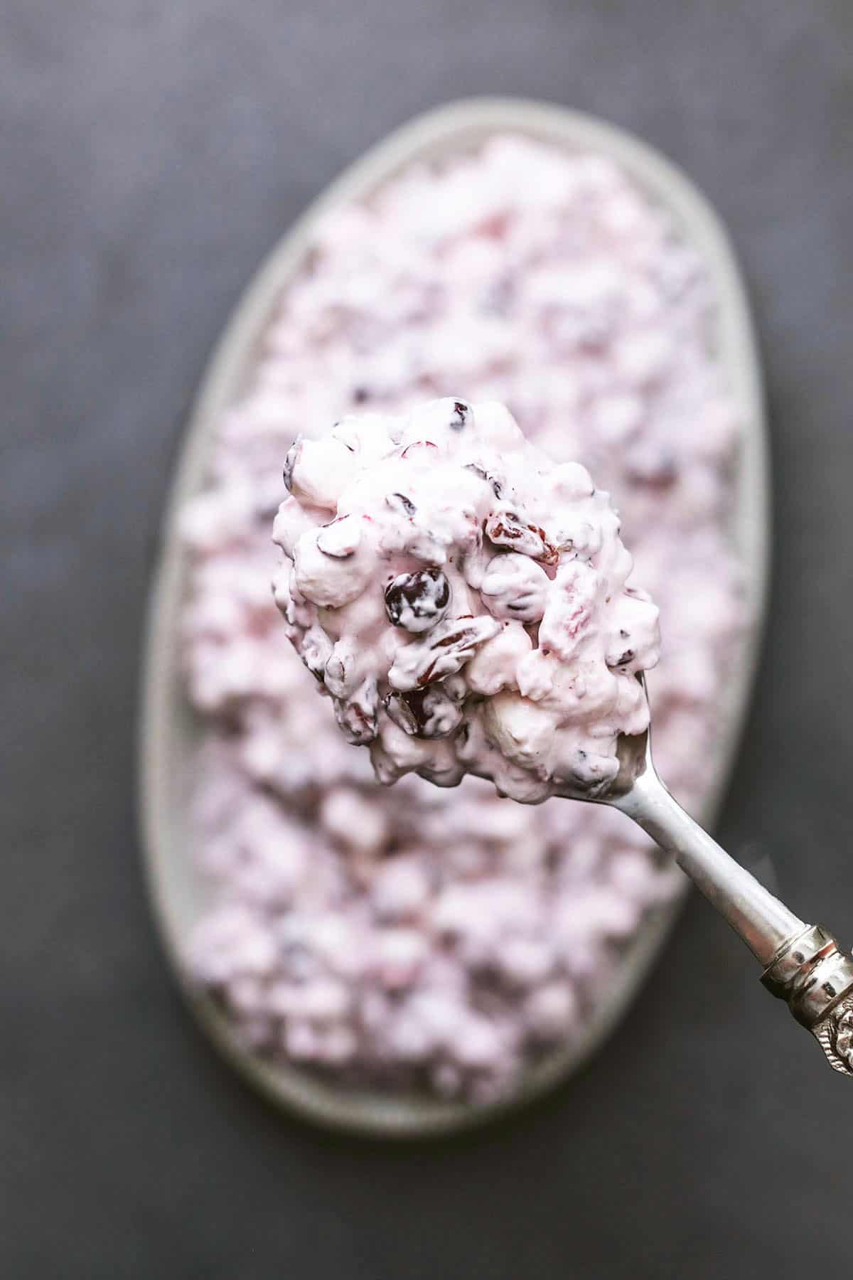 top view of a serving spoon full of cranberry salad above a platter of more salad.