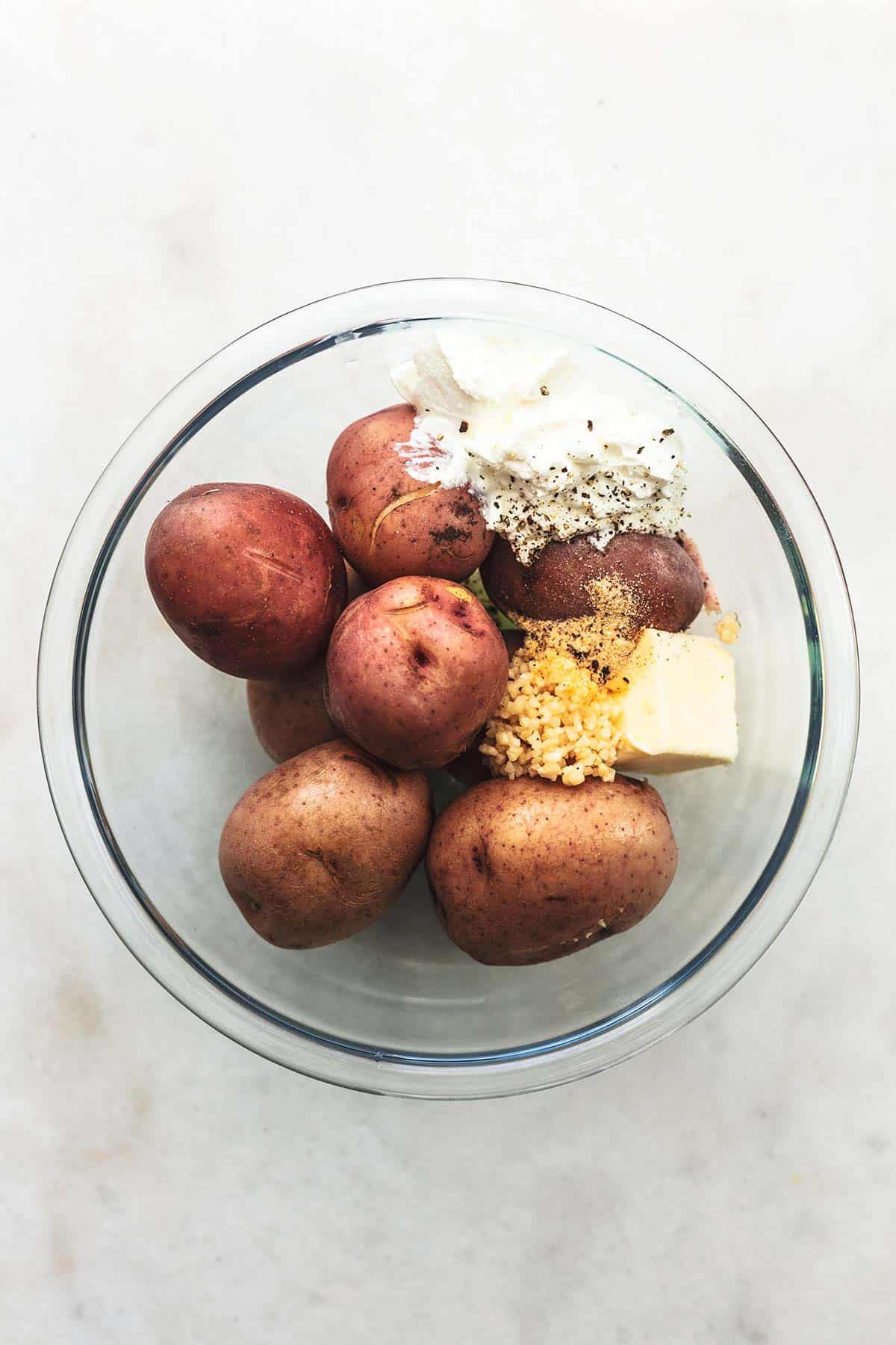 top view of potatoes, butter, sour cream, and garlic in a glass bowl.