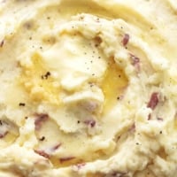 close up butter melting in mashed potatoes with some red skins and garlic