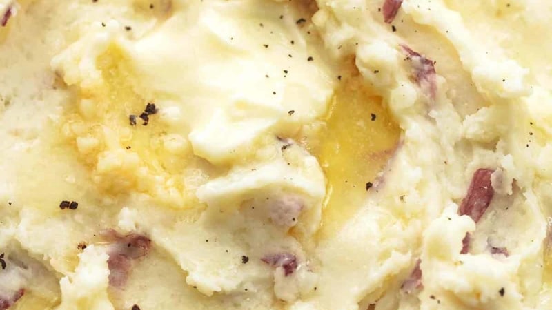 close up butter melting in mashed potatoes with some red skins and garlic