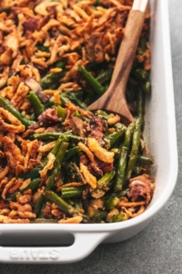 one corner of a white casserole dish filled with green bean casserole with wooden spoon