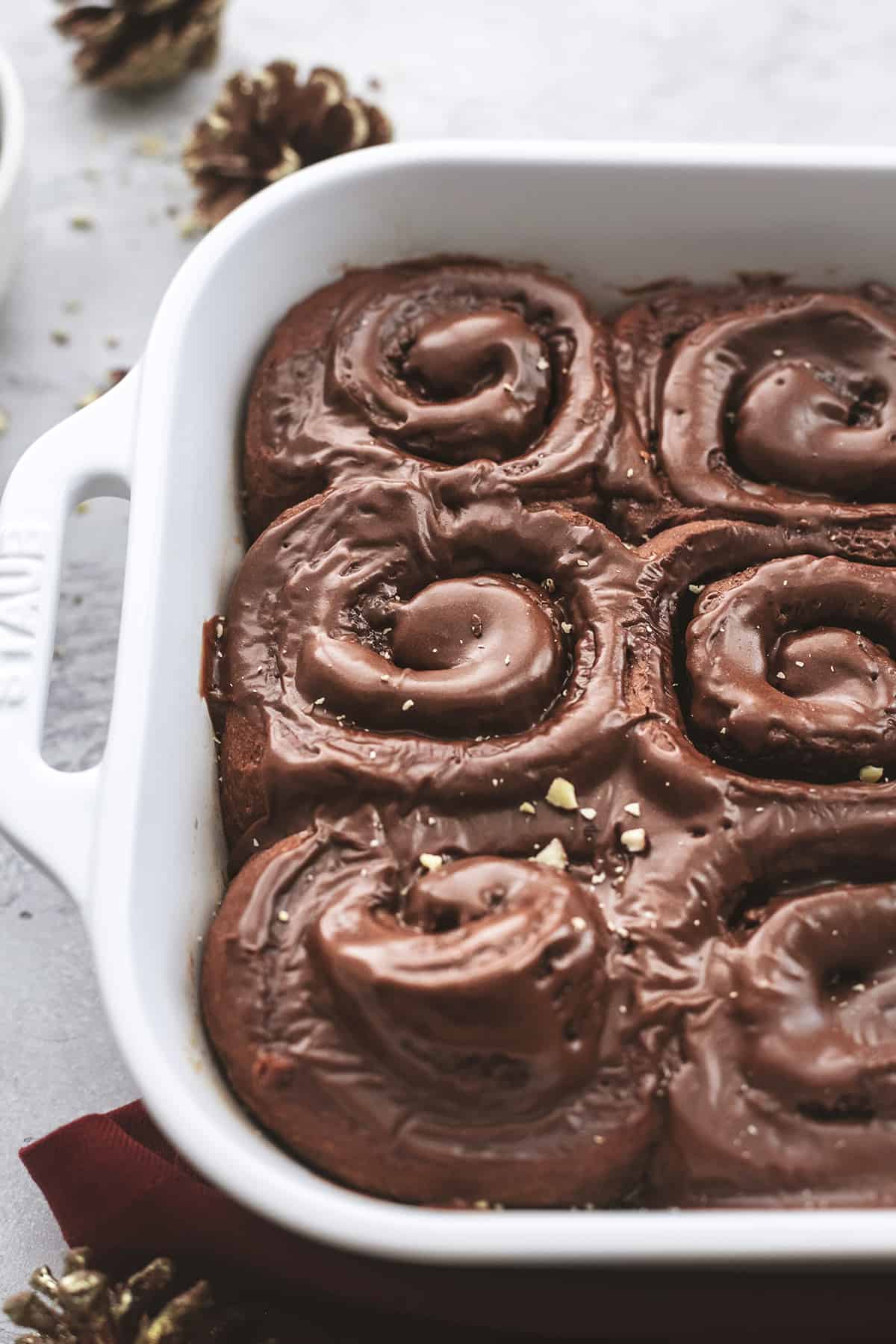 close up of chocolate cinnamon rolls with hazelnut icing in a baking pan.